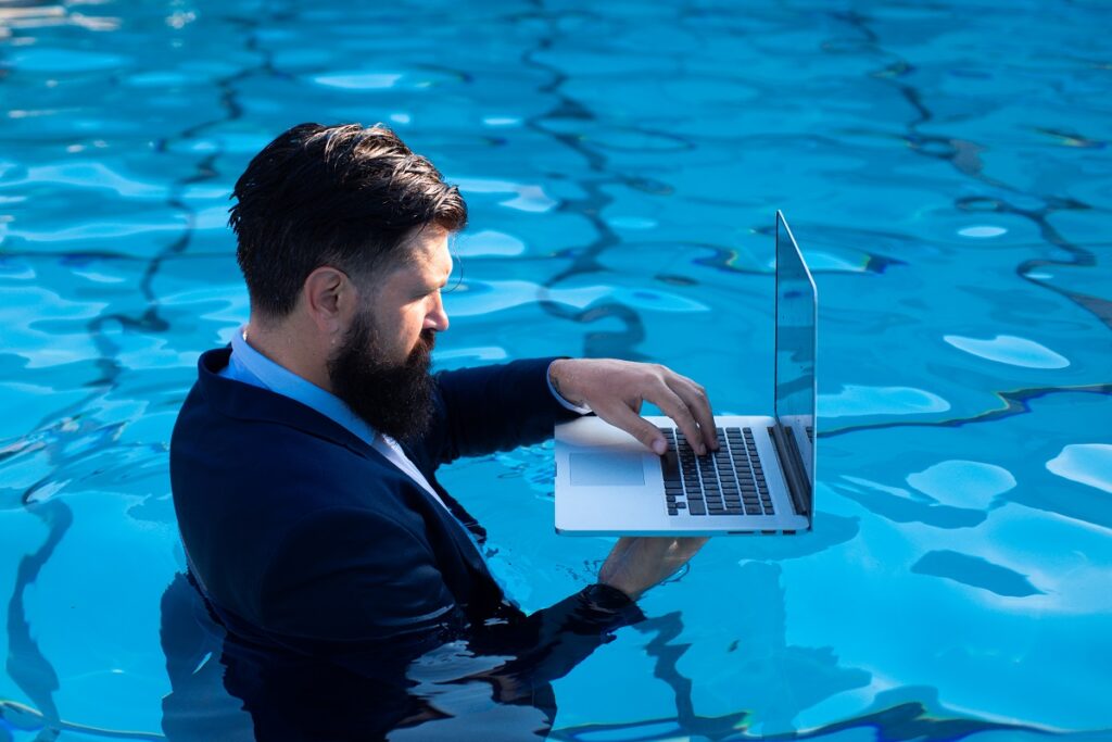 Business man in suit working on laptop from the swimming pool. Funny businessman relaxing with laptop