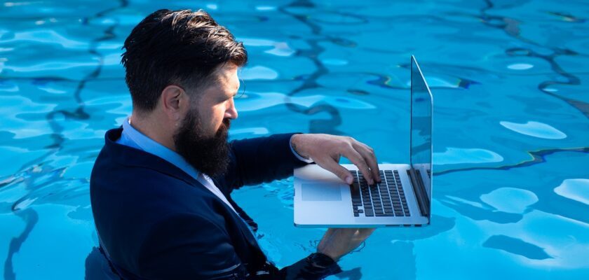 Business man in suit working on laptop from the swimming pool. Funny businessman relaxing with laptop