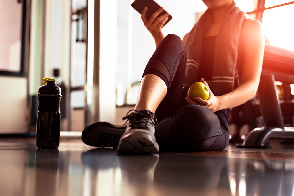 Woman using smart phone and holding apple while workout in fitness gym